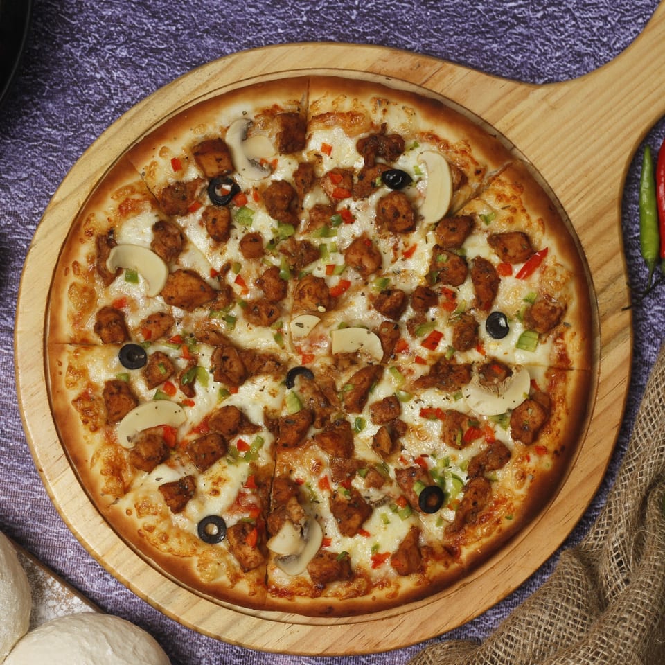 Mel's Roadhouse pizza with chicken, mushrooms, olives, and peppers on a wooden paddle.