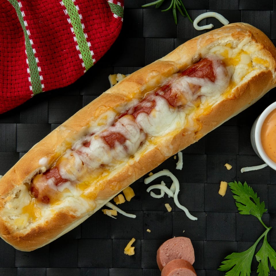 Mel's Roadhouse cheesy hot dog in a bun, with sauce, parsley, and sliced sausage.