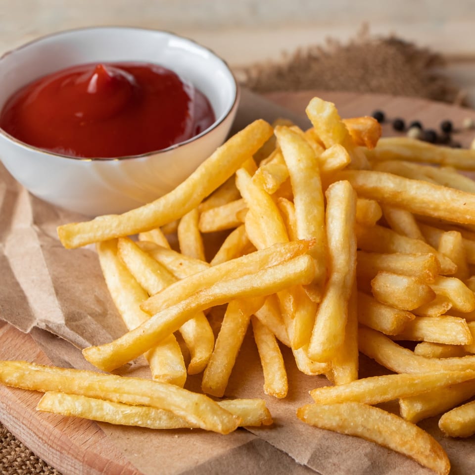 Golden french fries piled on brown paper with a white bowl of ketchup.