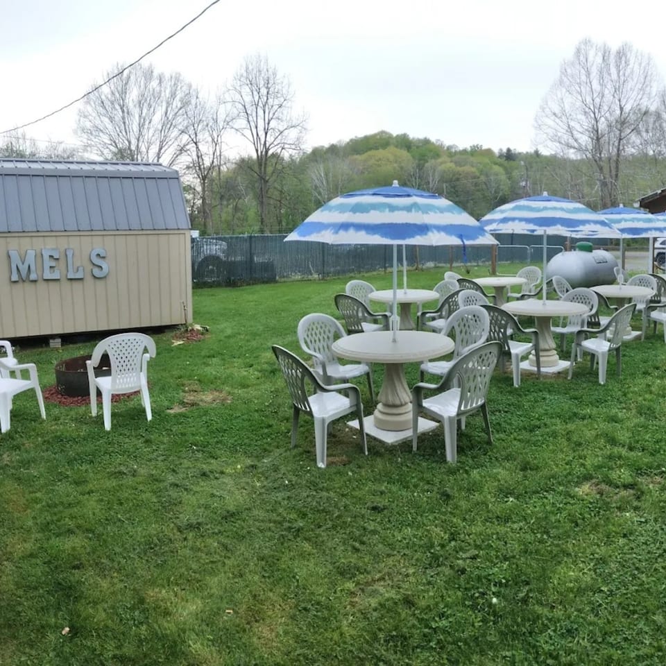 Mel's Roadhouse outdoor patio with white tables, chairs, and blue-and-white striped umbrellas on green grass.